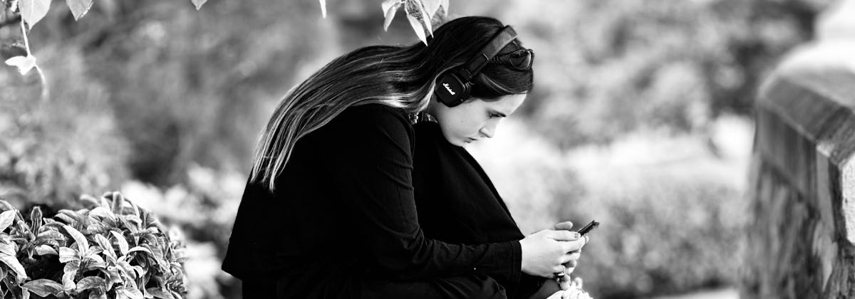Young woman listening to a slowed and reverb song on headphones with her smartphone outdoors