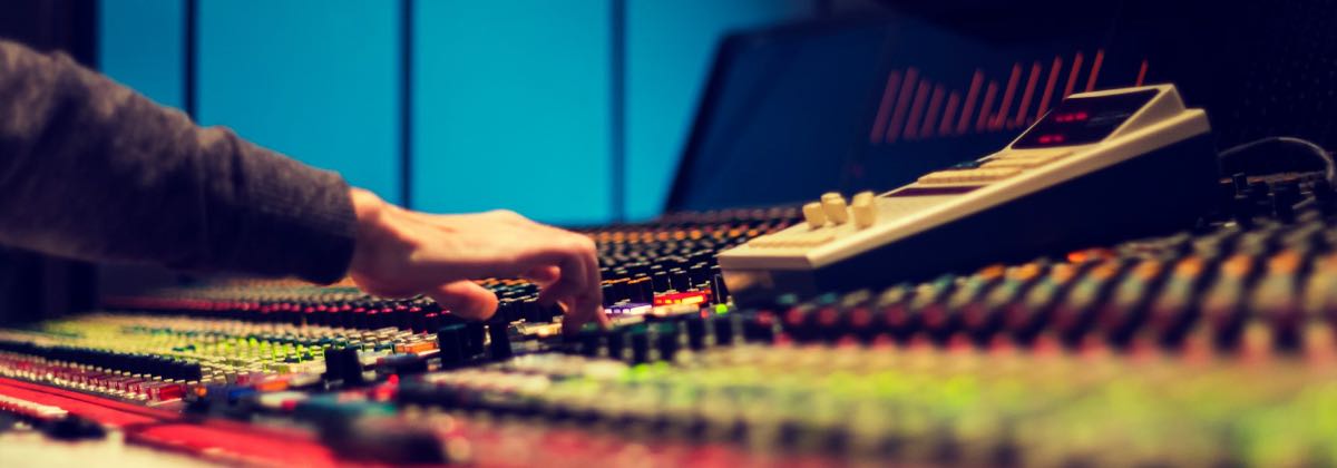Close-up of a hand adjusting equalizer knobs and faders on an audio mixing console